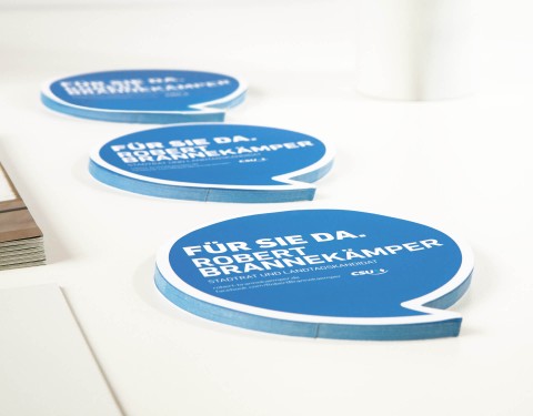 Drei Reihen der mit blauen Aufklebern in Sprechblasenform. Darauf befindet sich der Wahlspruch "Für Sie da. Robert Brannekämper.".